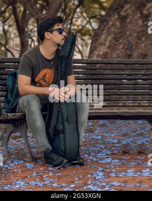 Gitarrist sitzt in einem Quadrat wartet mit seiner Gitarre in seinem Fall mit Blumen auf dem Boden vertikale Casual Kleidung Stockfoto