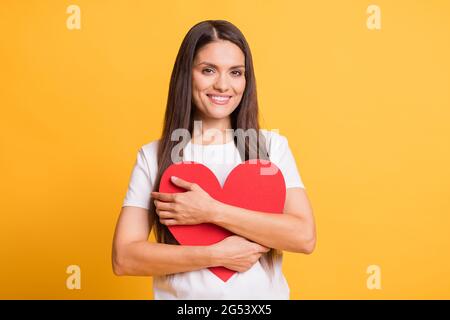 Foto-Porträt der Frau umarmt roten Papier Herz Liebe Symbol lächelnd Copyspace isoliert auf hellen gelben Hintergrund Stockfoto