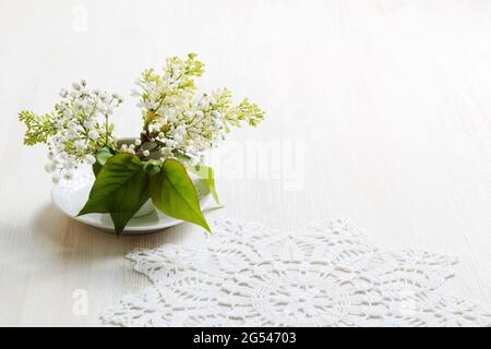 Zweig der blühenden Vogelkirsche (Prunus padus) in einer kleinen weißen Vase in der Nähe einer weißen Serviette auf einem weißen Holztisch Stockfoto