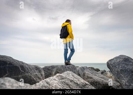 Frau in gelbem Regenmantel mit Blick auf das Meer, während sie auf Felsen steht Stockfoto