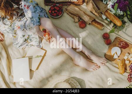 Schöne Beine einer jungen Frau in Weiß, die auf einer Decke sitzt und ein Picknick hat. Stockfoto