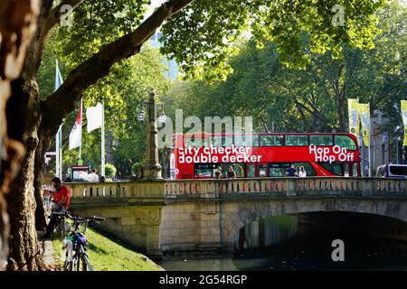 Rote Doppeldecker-Stadtrundfahrt 'Hop on / Hop off'-Bus auf einer Brücke über den Kö-Graben, den Stadtkanal an der Königsallee in Düsseldorf. Stockfoto