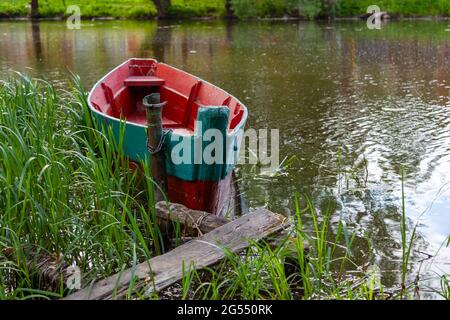 Ein altes grünes und rotes Holzboot kettete an einen Pfosten in der Nähe des Ufers. Stockfoto