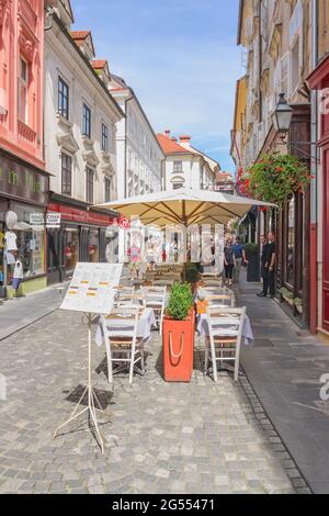 Ljubljana, Slowenien - 15. August 2018: Touristen und Restauranttische mit Sonnenschirmen teilen sich die malerische Stari-Straße in der Altstadt Stockfoto