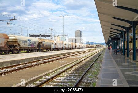 Ljubljana, Slowenien - 15. August 2018: Ein langer Güterzug fährt durch den Hauptbahnhof, während einige Passagiere auf ihren Transport warten Stockfoto