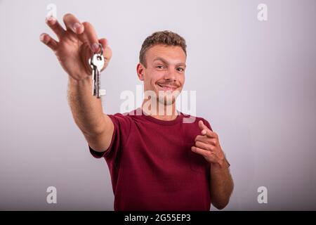 Ein auf weißem Hintergrund isolierter Junge hält Schlüssel in der Hand und zeigt auf sie, Werbefoto, Immobilienmakler-Konzept, Stockfoto