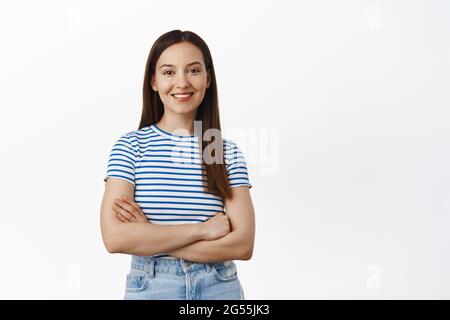 Junge Profis. Glückliche Frau sieht selbstbewusst aus, kreuzt die Arme auf der Brust und schaut in die Kamera, selbstbewusste, entschlossene Pose, steht in T-Shirt und Jeans Stockfoto