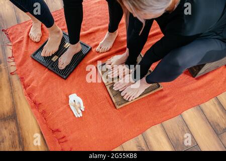 Frauen lernen, wie man mit scharfen Metallnägeln auf dem Sadhu-Brett steht. Yoga und Gesundheitskonzept Stockfoto
