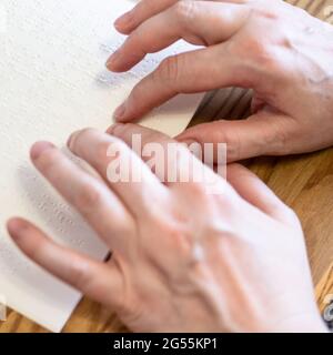 Frau las Buch mit Braille an den Fingerspitzen aus der Nähe auf einem bewaldeten Tisch Stockfoto