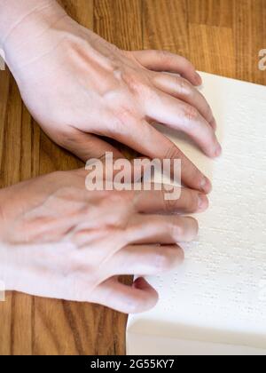 Ansicht der weiblichen Finger beim Lesen des Buches mit Braille-Nahaufnahme auf einem bewaldeten Tisch Stockfoto