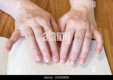Vorderansicht der weiblichen Finger beim Lesen des Buches mit Braille-Nahaufnahme auf einem bewaldeten Tisch Stockfoto