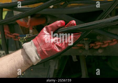 Die Hand eines Mannes in einem Gummihandschuh hält einen Wasserschlauch. Der Schlauch muss am Sprinkler befestigt werden. Stockfoto