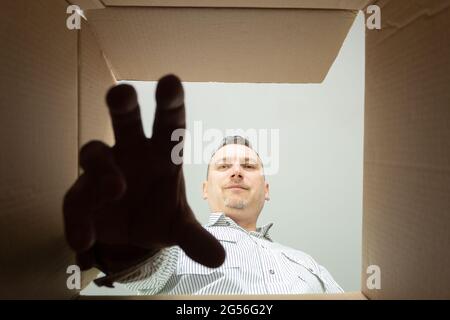 Der Mann nimmt den Gegenstand aus dem Karton. Ansicht von unten. Holen Sie sich etwas aus einem Karton Stockfoto