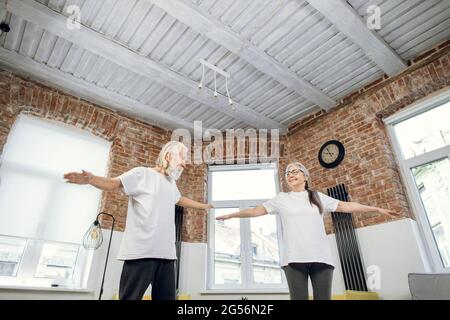 Lächelnde, gealterte Frau und Mann in Sportkleidung, die zu Hause die Morgenübungen machen. Glückliches Paar Workout zusammen. Konzept des aktiven Ruhestandes. Stockfoto