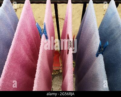 Nahaufnahme von rosa und blauen Handtüchern, die mit bunten Wäscheklammern an den Seilen hängen Stockfoto