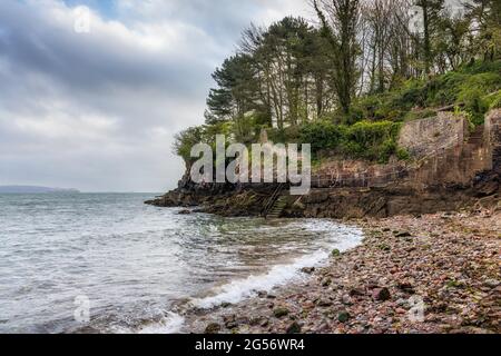 An der Küste von Brixham in Devon gelegen, ist Fishcombe Cove ein kleiner Kiesstrand und eine Bucht, die von allen Seiten durch hohe rote Klippen geschützt ist. Stockfoto