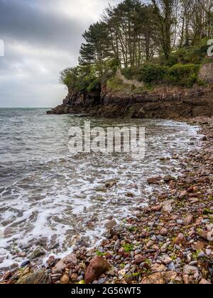 An der Küste von Brixham in Devon gelegen, ist Fishcombe Cove ein kleiner Kiesstrand und eine Bucht, die von allen Seiten durch hohe rote Klippen geschützt ist. Stockfoto