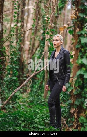 Mode an ungewöhnlichen Orten, Junge Frau in edgy Motorrad Jacke im Wald Stockfoto