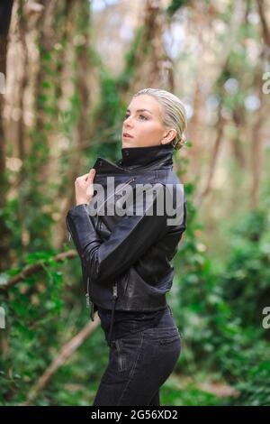 Mode an ungewöhnlichen Orten, Junge Frau in edgy Motorrad Jacke im Wald Stockfoto
