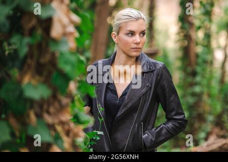 Mode an ungewöhnlichen Orten, Junge Frau in edgy Motorrad Jacke im Wald Stockfoto
