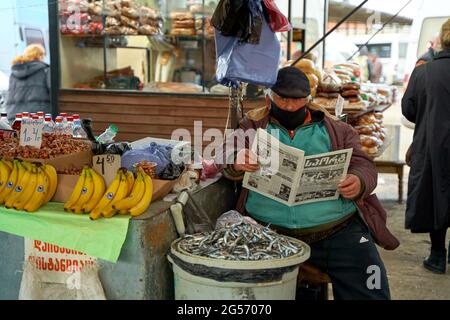 Übergewichtiger georgischer Mann. Ein Straßenmarktverkäufer liest eine Zeitung, während er an der Theke sitzt. Stockfoto