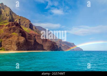 Blick auf einen Regenbogen vor Kauais zerklüfteter Nā Pali Coast, wo Kauais zerklüftete, abgelegene Küste auf den Pazifischen Ozean trifft Stockfoto