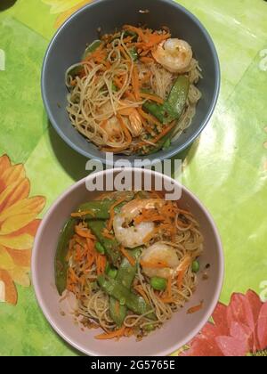 Wok-Nudeln mit Gemüse und Garnelen aus der asiatischen Küche auf rosa und grauen Tellern Stockfoto