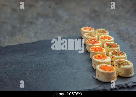 Käseplatte mit Gewürzen. Mazzarella Käse mit verschiedenen Gewürzen. Käsesnacks verschiedener Geschmacksrichtungen auf einem Tablett aus schwarzem Stein. Hintergrund oder Banner auf t Stockfoto