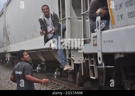 Menschen werfen Essen an Mittelamerikaner, die im Zug vorbeifahren, den sie La Bestia nennen. Stockfoto