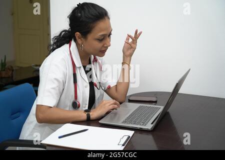 Eine südindische Ärztin in den 30er Jahren mit Laptop und Verordnungsplatine mit weißem Mantel und rotem Stethoskop auf weißem Hintergrund.Online-medizinische Beratung Stockfoto