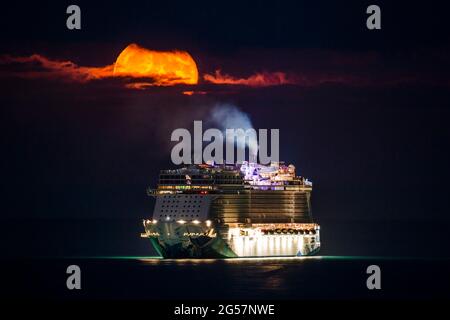 Weymouth, Dorset, Großbritannien. Juni 2021. Wetter in Großbritannien. Der fast volle Erdbeer-Supermond leuchtet orange, während er durch einen kleinen Wolkenbruch über dem leeren NCL-Kreuzschiff Norwegian Escape, das in der Bucht von Weymouth in Dorset vor Anker liegt, leuchtet. Bildnachweis: Graham Hunt/Alamy Live News Stockfoto