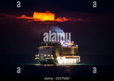 Weymouth, Dorset, Großbritannien. Juni 2021. Wetter in Großbritannien. Der fast volle Erdbeer-Supermond leuchtet orange, während er durch einen kleinen Wolkenbruch über dem leeren NCL-Kreuzschiff Norwegian Escape, das in der Bucht von Weymouth in Dorset vor Anker liegt, leuchtet. Bildnachweis: Graham Hunt/Alamy Live News Stockfoto