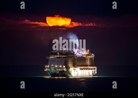 Weymouth, Dorset, Großbritannien. Juni 2021. Wetter in Großbritannien. Der fast volle Erdbeer-Supermond leuchtet orange, während er durch einen kleinen Wolkenbruch über dem leeren NCL-Kreuzschiff Norwegian Escape, das in der Bucht von Weymouth in Dorset vor Anker liegt, leuchtet. Bildnachweis: Graham Hunt/Alamy Live News Stockfoto