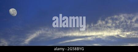 Eine lebhafte atmosphärische Wolkenlandschaft mit weißen Altostratus-Wolken und einem abnehmenden Mond in einem mittelblauen Himmel. Schönheit in der Natur. Neu Stockfoto