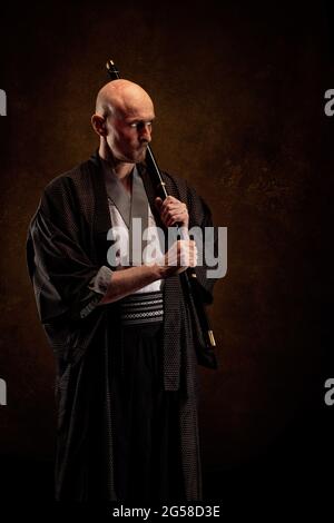 Ansicht eines blinden und kahlen Mannes, der einen Kimono trägt und ein Katana in den Händen hält Stockfoto