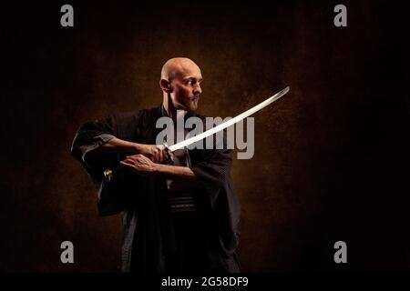 Ansicht eines blinden und kahlen Mannes, der einen Kimono trägt und ein Katana in den Händen hält Stockfoto