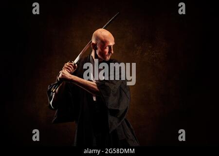 Ansicht eines blinden und kahlen Mannes, der einen Kimono trägt und ein Katana in den Händen hält Stockfoto