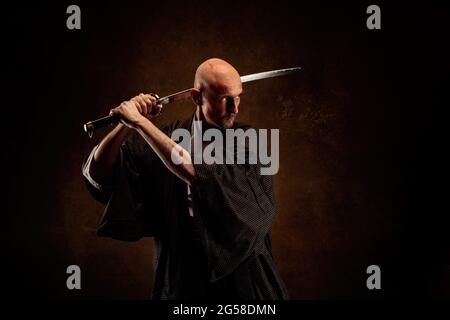 Ansicht eines blinden und kahlen Mannes, der einen Kimono trägt und ein Katana in den Händen hält Stockfoto