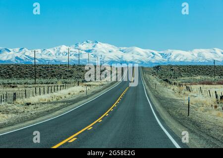 USA, Nevada, Winnemucca, Highway 95 durchquert Wüstenlandschaft mit schneebedeckten Bergen in der Ferne Stockfoto