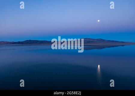 USA, Nevada, Hawthorne, Calm Walker Lake, der den Mond in der Abenddämmerung reflektiert Stockfoto