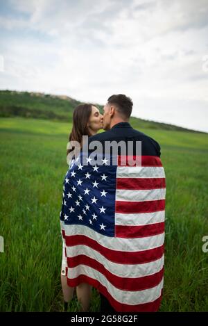 Junges Paar eingewickelt in amerikanische Flagge küssen in Weizenfeld Stockfoto