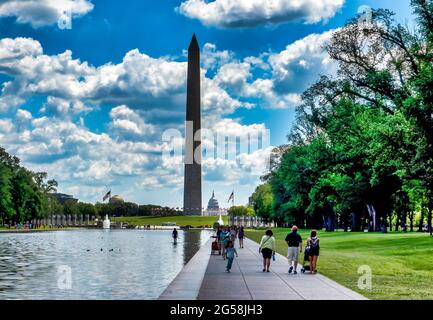 Besucher spazieren entlang des reflektierenden Pools in Washington D.C., mit dem Denkmal des Zweiten Weltkriegs und dem Kapitolgebäude im Hintergrund Stockfoto