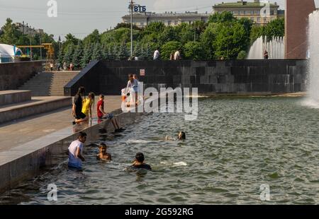 Gekleidete Teenager baden in einem Wasserreservoir auf einem großen Platz in der Stadt, um sich während der Hitzewelle zu erfrischen und die Temperaturen erreichen Rekordwerte Stockfoto