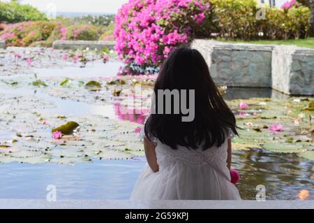 Kleines Mädchen, das in einem Resort in Bali, Indonesien, am Seerosenblumenteich sitzt Stockfoto