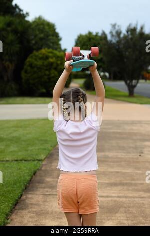 Das junge Mädchen hält Skateboard über Kopf und läuft einen Fußweg hinunter Stockfoto