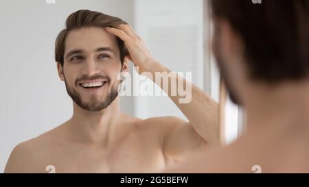 Glücklich schöner junger Kerl kämmen glatte braune Haare mit den Fingern Stockfoto