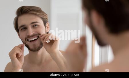 Glücklich gut aussehend junger Kerl putzen weiße Zähne mit Zahnseide Stockfoto