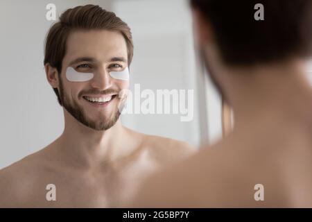 Glücklicher, hübscher junger Mann, der weiße Flecken mit Kollagen-Gel-Flecken anwendet Stockfoto