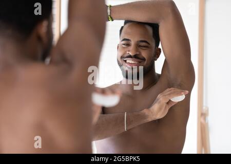 Ruhiger, hübscher junger, gut gebauter Mann, der Deodorant verwendet und Antitranspirant anwendet Stockfoto