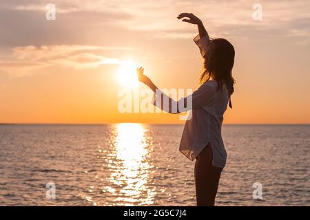 Silhouette einer jungen glücklichen unbeschwerten Frau, die bei Sonnenuntergang am Strand posiert Stockfoto